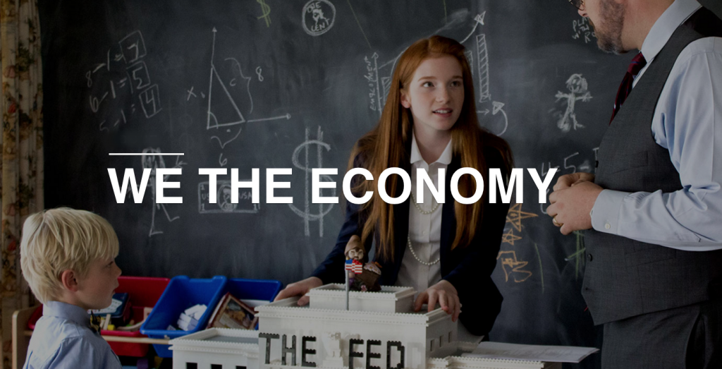 We The Economy: three people in a classroom stand around a model of the US Federal Reserve