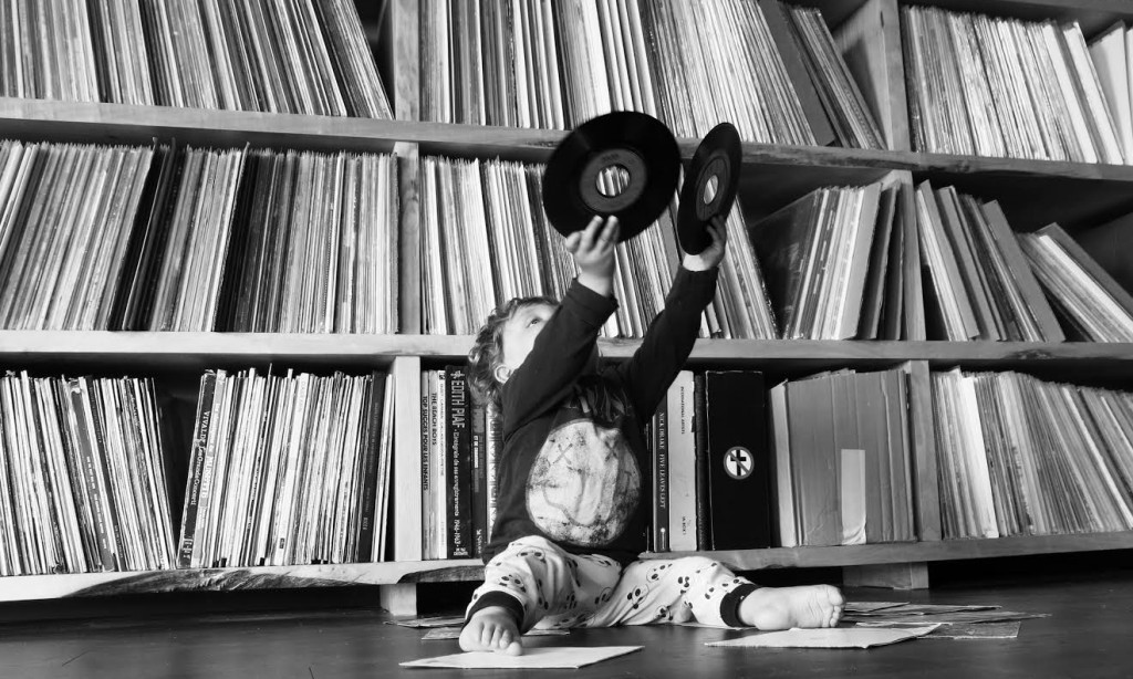 A small child sat on the floor holds up two vinyl records