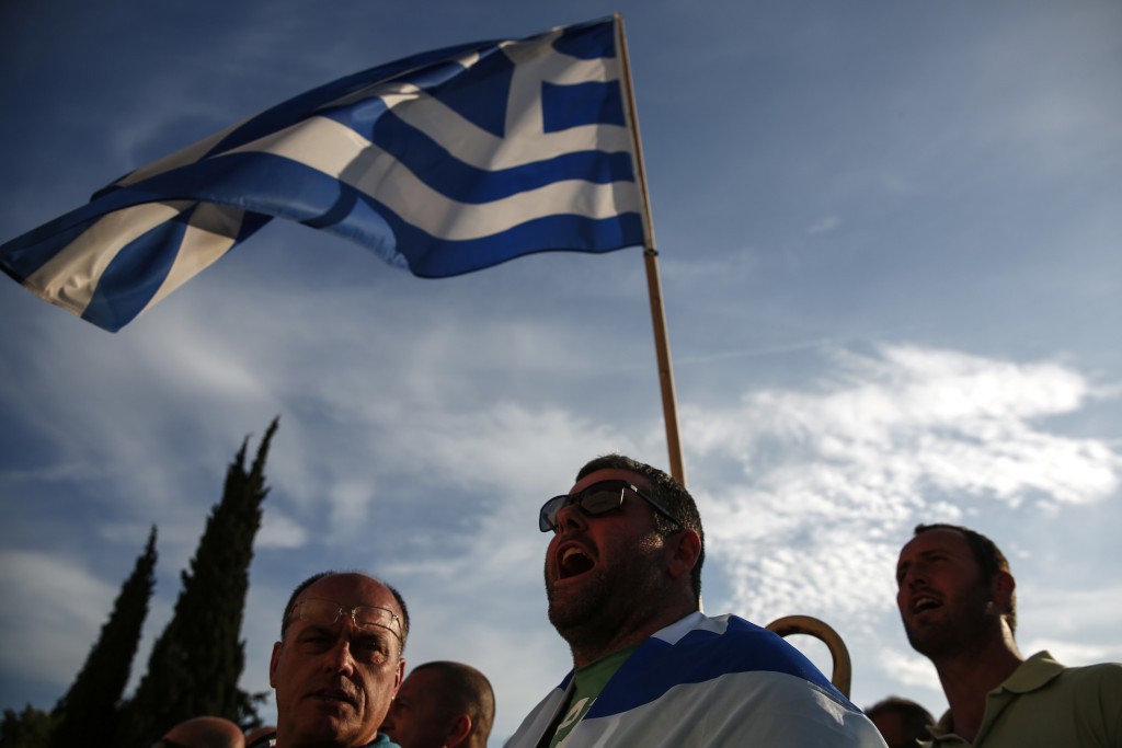 Protesters in Greece stand in front of a Greek flag