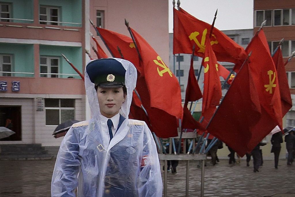 A North Korean traffic police woman directs vehicles at a street junction while behind her the sidewalk is decorated with flags of the ruling party