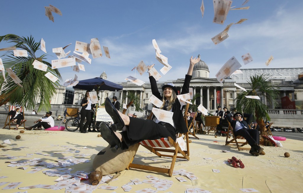A protestor throws fake money into the air as she relaxes on a deckchair in an interactive, tropical tax haven beach in Trafalgar Square in London