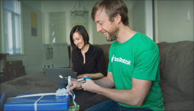 A Taskrabbit worker wraps a present, while a woman sits next to him working on her laptop