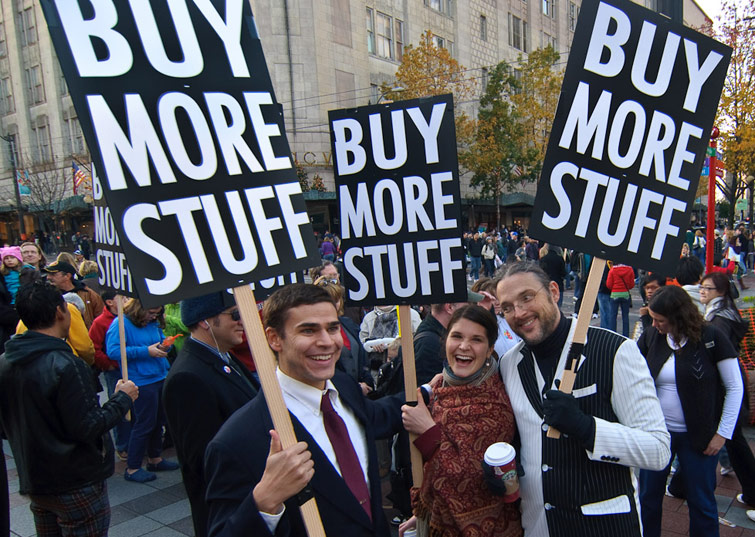 People hold placards that say 'Buy More Stuff'