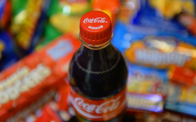 A bottle of Coca Cola with biscuits, crisps, chocolate bars and carbonated drinks