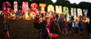A festival-goer blowing bubbles in front of the Glastonbury sign at the Glastonbury Festival