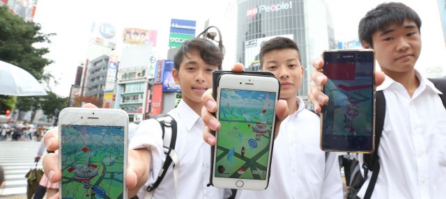 Three teenage boys hold up their phones while playing Pokemon Go