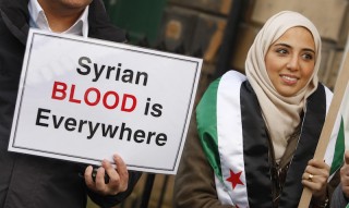 A man and woman hold a sign saying 'Syrian blood is everywhere'