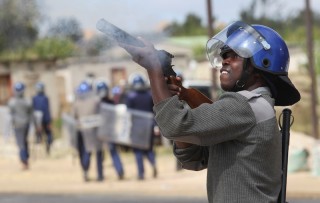 Armed policeman fires a tear gas gun in Zimbabwe Riots