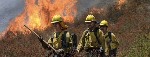 California Firefighters walk ahead of flames engulfing the bush