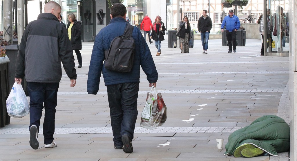 Shoppers pass a homeless man in Manchester