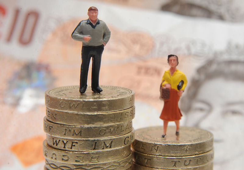 Two plastic models, one man, one woman, stand on top of piles of pound coins