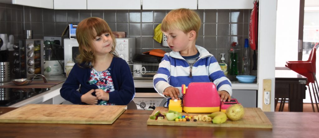 Two young children playing with food in a kitchen
