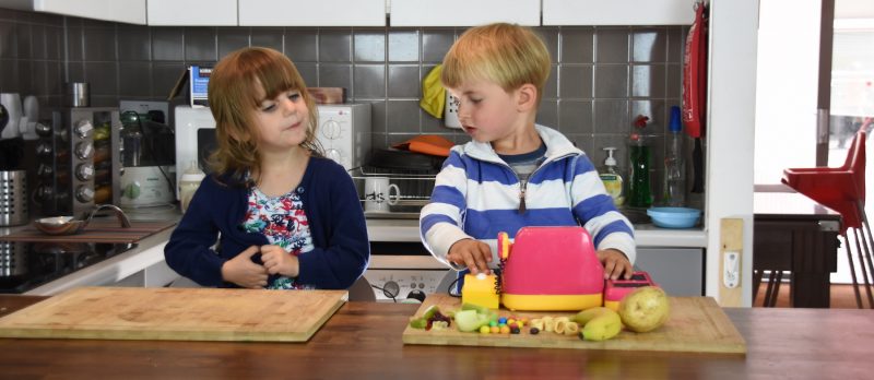 Two young children playing with food in a kitchen