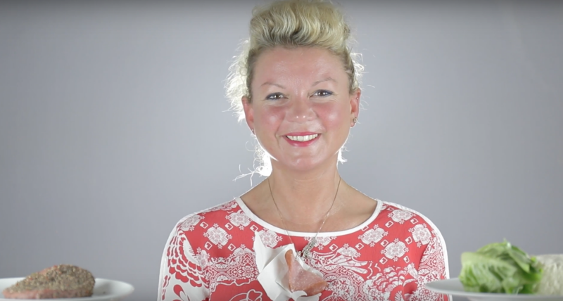 A smiling woman sits between a meat based meal and a vegan meal