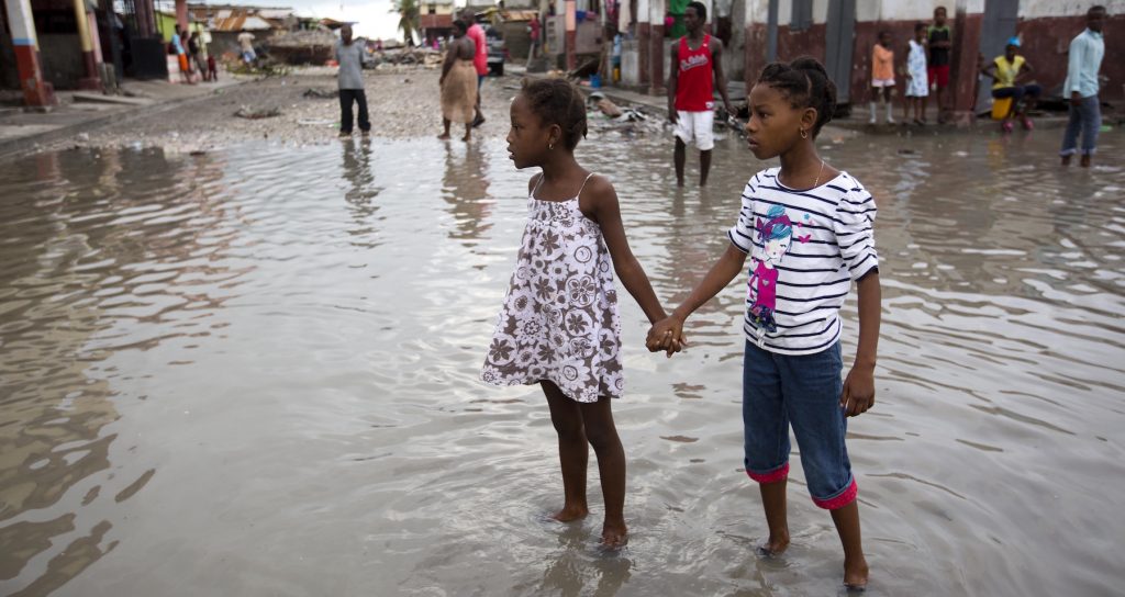 Two young girls stand holding hands in a flooded street