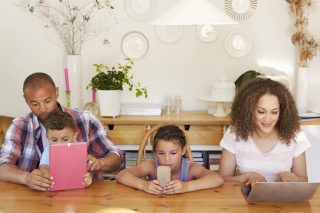 Family Sitting Around Table At Home Using Technology