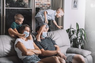 mom-and-dad-are-wearing-facial-surgical-masks-two-little-sons-are-jumping-over-parents-sitting-on-the_t20_nLgdGP