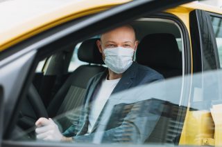 bald-man-taxi-driver-in-medical-face-mask-inside-yellow-car-looks-at-camera-concept-of-coronavirus_t20_R01yda