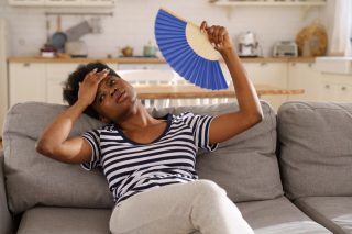 tired-african-american-woman-suffering-from-heatstroke-flat-without-air-conditioner-waving-blue-fan_t20_OJV2JE