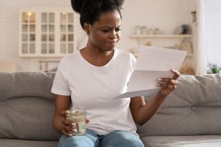 depressed-sad-black-girl-holding-last-cash-money-and-papers-calculate-domestic-bills-at-home-african_t20_9kY8O6