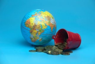 selective-focus-of-world-globe-and-a-red-bucket-with-a-gold-coins-isolated-on-a-blue-background_t20_2Wwl06