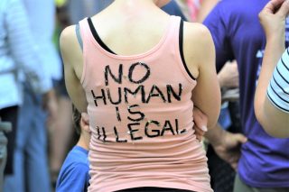 millennial-wearing-a-t-shirt-at-a-protest-rally-no-human-is-illegal-news-media-families-belong_t20_LOg6Vo