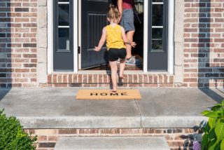 little-girl-walking-up-the-steps-in-a-new-home-with-a-welcome-mat-in-a-surburban-residential_t20_R0vWQk